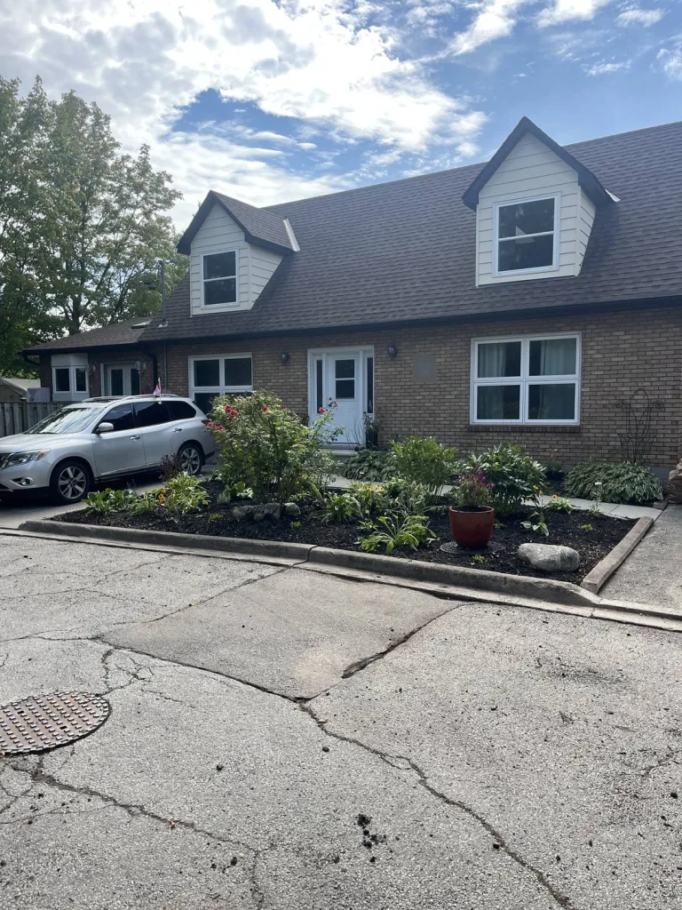 Curbed front garden with hostas, flowering shrubs and a terracotta planter in front of a brick Cape Cod house in Ancaster