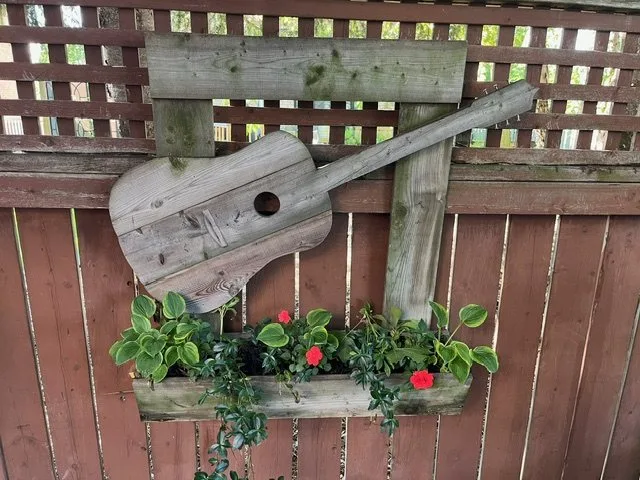 Rustic wooden guitar and a window box of red impatiens mounted on a lattice-top cedar fence in Stoney Creek